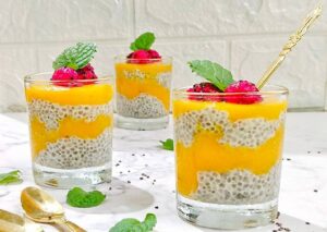 A glass of creamy mango chia pudding topped with fresh fruit, showcasing a healthy and delicious dessert.